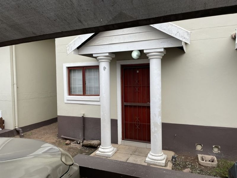 Front entrance of the apartment featuring a covered porch with decorative columns and a security gate.