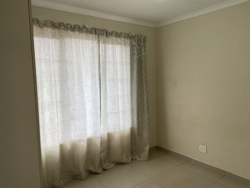 A simple, empty bedroom featuring neutral tiled flooring, cove cornicing, and a window with installed curtain tracks.
