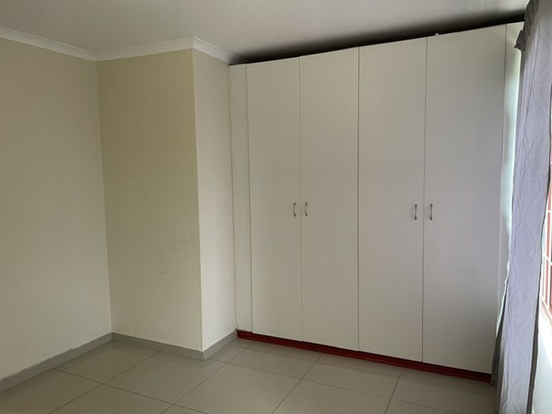 A clean and bright bedroom featuring neutral walls, tiled flooring, and ample built-in cupboard storage space.