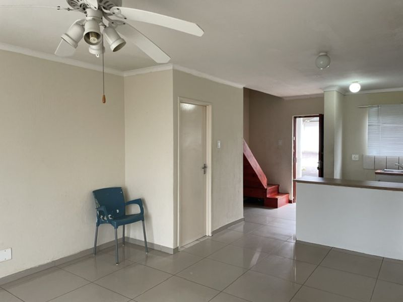 An open-plan living and kitchen area featuring tiled flooring, a ceiling fan, and a staircase leading to an upper level.