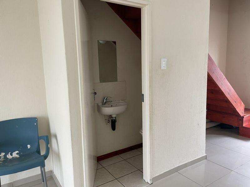 A compact guest bathroom featuring a wall-mounted basin, tiled flooring, and adjacent staircase access within an open-plan living area.
