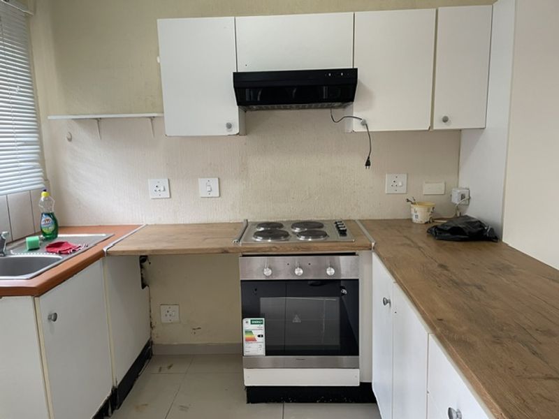 A compact kitchen featuring laminate countertops, built-in cabinetry, and integrated oven and hob. The space requires cosmetic updates to improve its overall condition.
