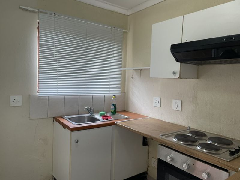 A compact kitchen featuring built-in cabinetry, an electric hob with extractor fan, and a stainless steel sink, requiring cosmetic updates to improve its condition.