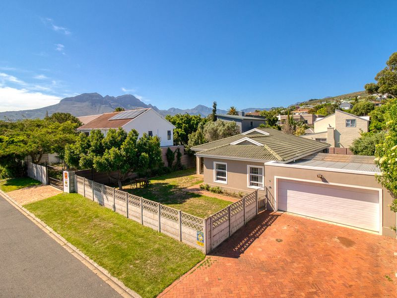 Aerial view of a residential property featuring a paved driveway, double garage, front garden with lawn, and secure boundary walling.