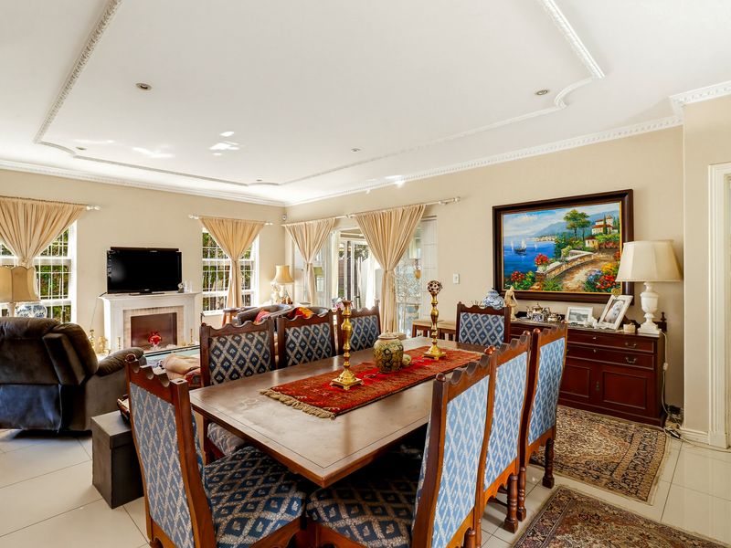 Spacious open-plan living and dining area featuring tiled floors, decorative ceiling molding, a fireplace, and large windows providing natural light.