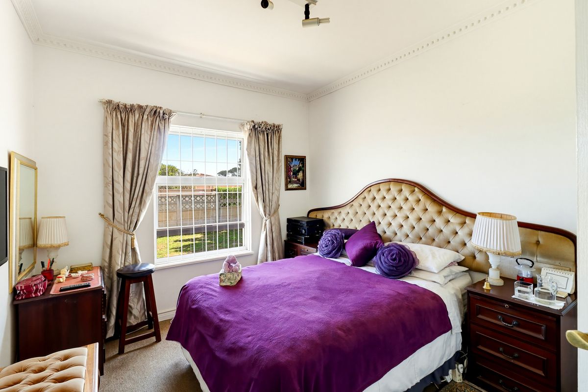 A well-lit bedroom featuring crown molding, carpeted flooring, and a window with security bars overlooking the rear garden area.