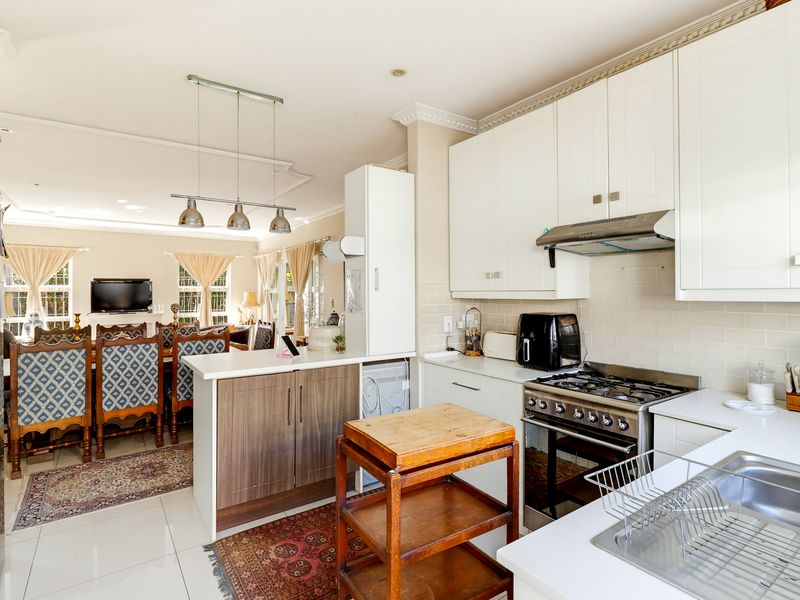 An open-plan kitchen and dining area featuring white cabinetry, a gas stove, subway tile backsplash, and elegant crown molding throughout the space.