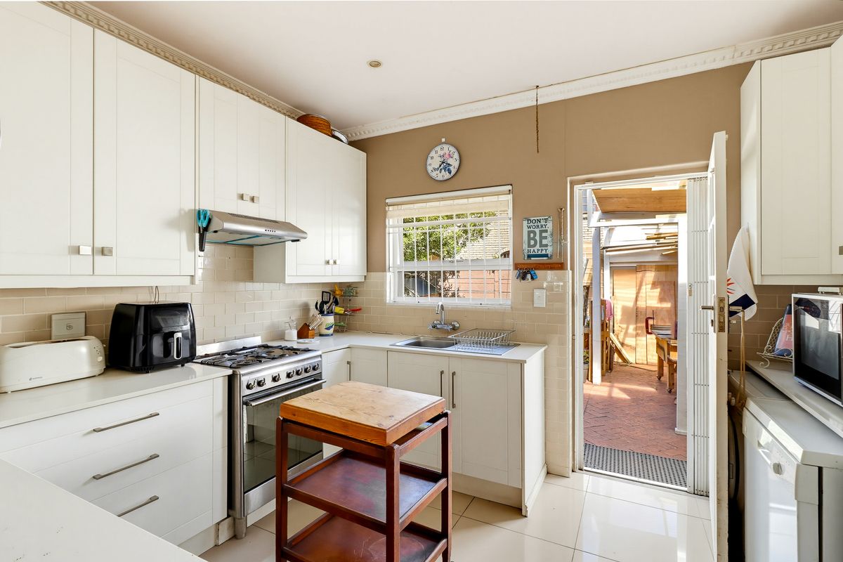 A functional kitchen featuring white cabinetry, a gas stove with extractor fan, tiled backsplash, and direct access to an outdoor patio area.