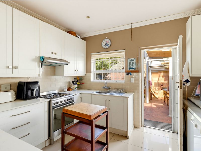 A functional kitchen featuring white cabinetry, a gas stove with extractor fan, tiled backsplash, and direct access to an outdoor patio area.