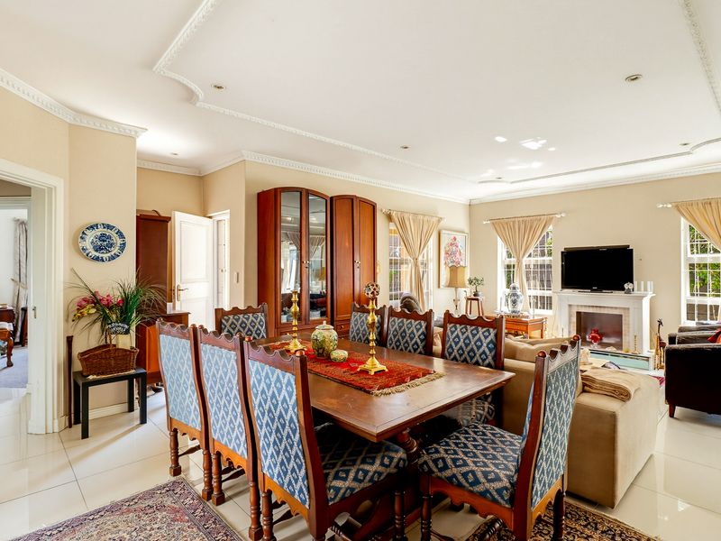 Spacious open-plan living and dining area featuring tiled flooring, decorative ceiling cornices, recessed lighting, and a central fireplace.
