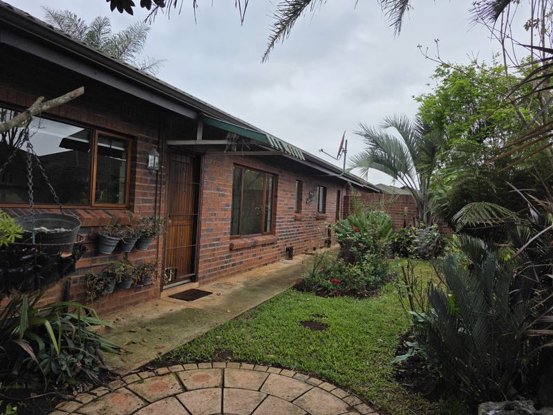 A rear exterior view of a face brick retirement unit featuring a paved walkway, established garden, and timber-framed windows.