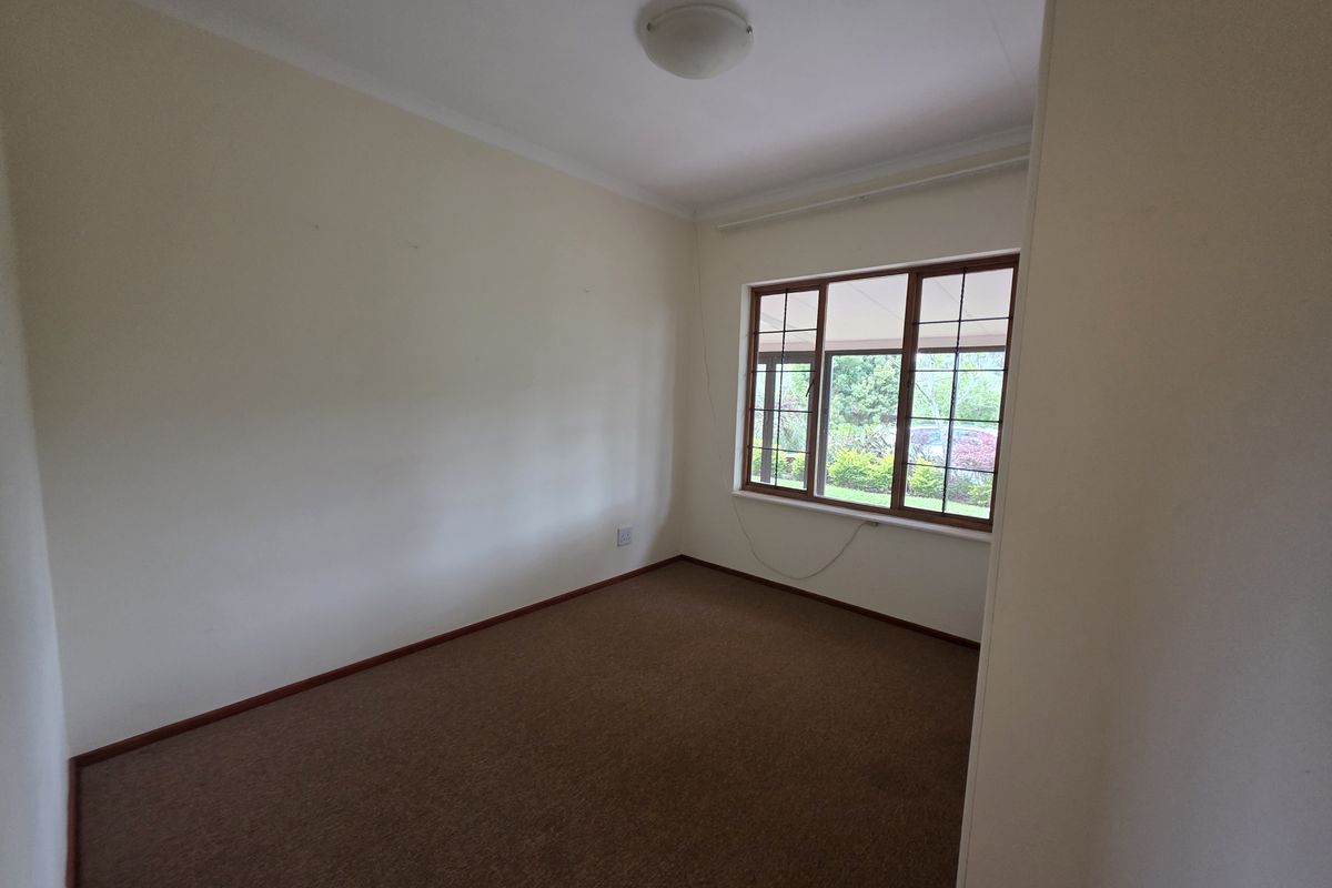 A vacant bedroom featuring neutral walls, carpeted flooring, and large timber-framed windows providing natural light and garden views.