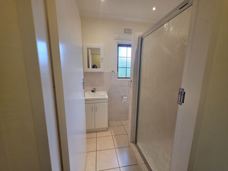 A functional bathroom featuring a vanity unit with basin, a shower enclosure, and neutral wall and floor tiling.