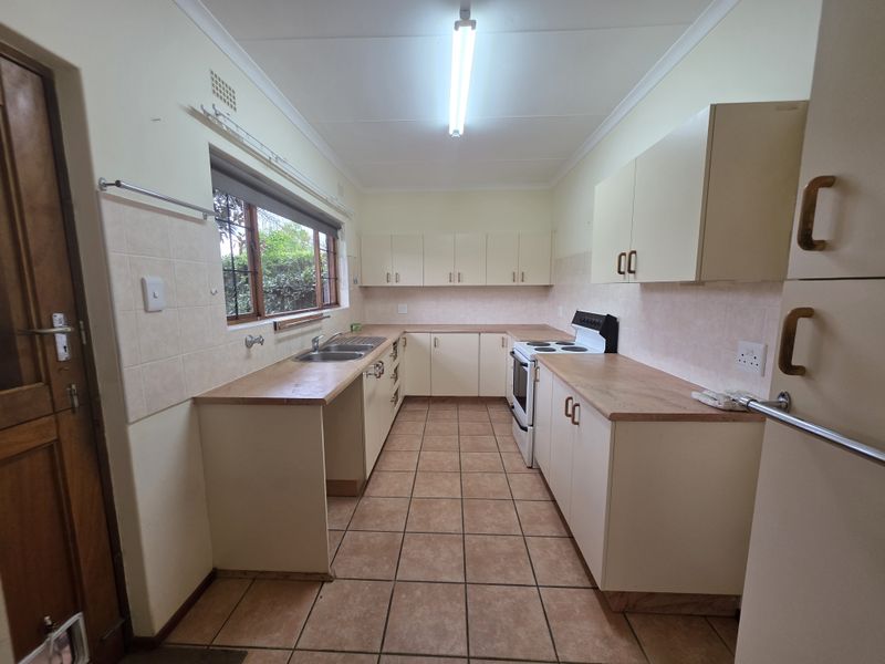 A functional kitchen featuring laminate countertops, ample built-in cabinetry, a double bowl sink, and a freestanding stove with tiled flooring.