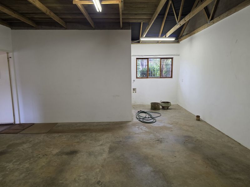 An unfinished, spacious garage area featuring exposed timber roof trusses, concrete flooring, and a window with security bars.