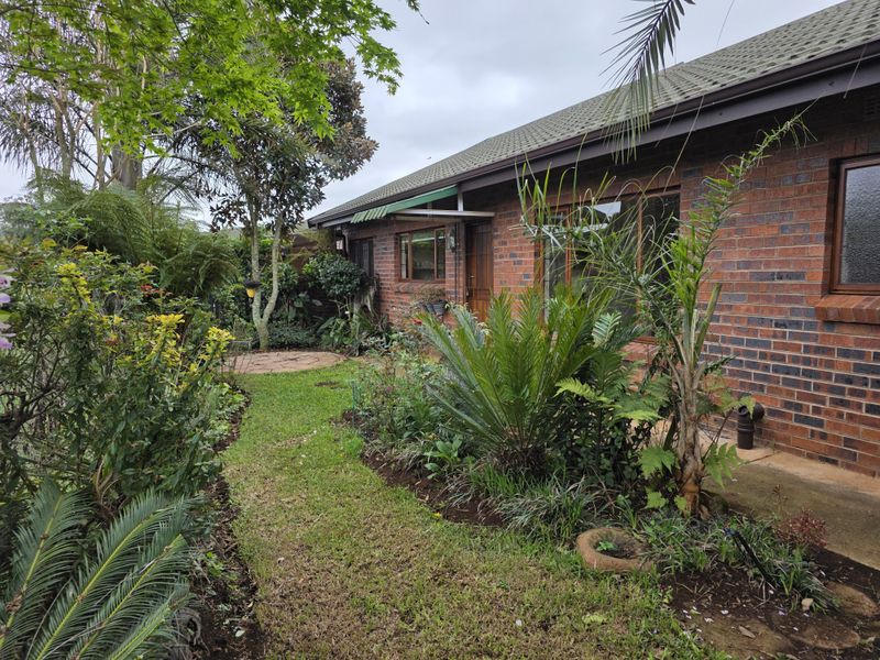 A well-maintained rear exterior view of a brick retirement unit featuring a paved patio, established garden, and tiled roof.