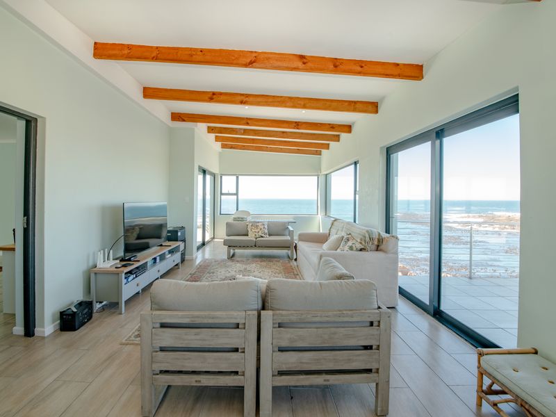 Bright and airy living room featuring exposed timber ceiling beams, large sliding glass doors, and expansive ocean views.