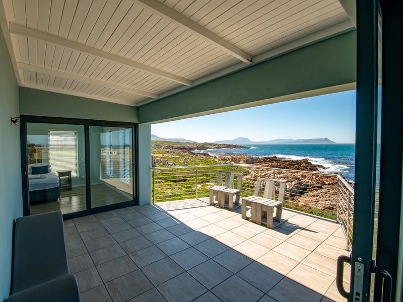 A spacious covered balcony featuring tiled flooring and a stainless steel balustrade, offering panoramic ocean and coastal views.