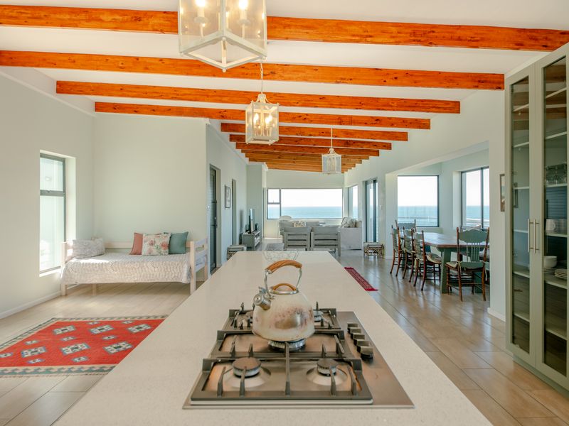 Spacious open-plan living area featuring exposed timber ceiling beams, a central kitchen island with a gas hob, and expansive windows with ocean views.