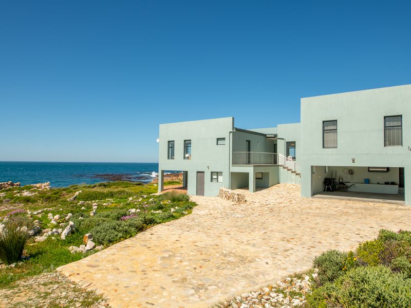 A modern coastal residence featuring a stone-paved driveway, integrated garage, and balcony, set against a scenic oceanfront landscape.