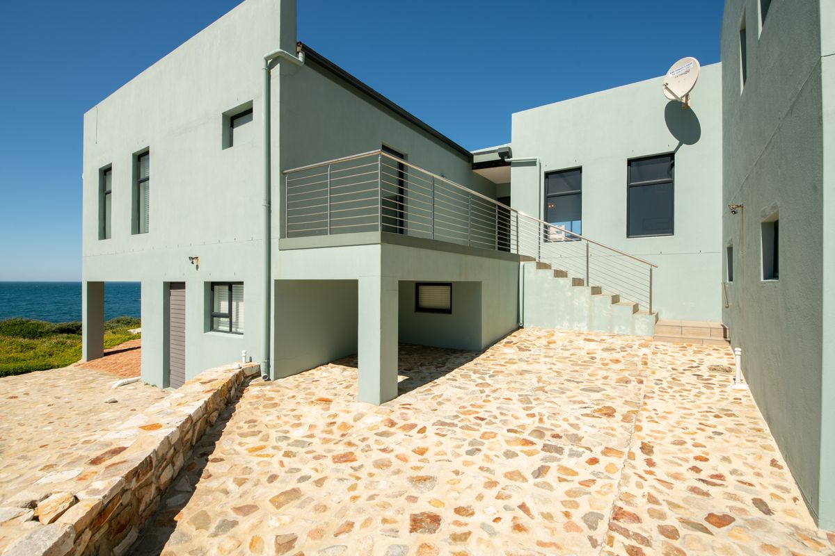 Rear exterior view of the property featuring a stone paved patio, external staircase with stainless steel balustrade, and coastal views.