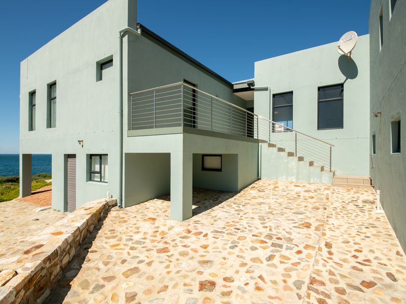 Rear exterior view of the property featuring a stone paved patio, external staircase with stainless steel balustrade, and coastal views.