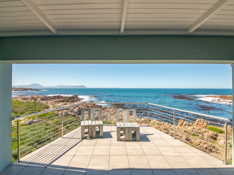 A covered patio featuring tiled flooring and a stainless steel balustrade, offering expansive, unobstructed ocean and coastal views.