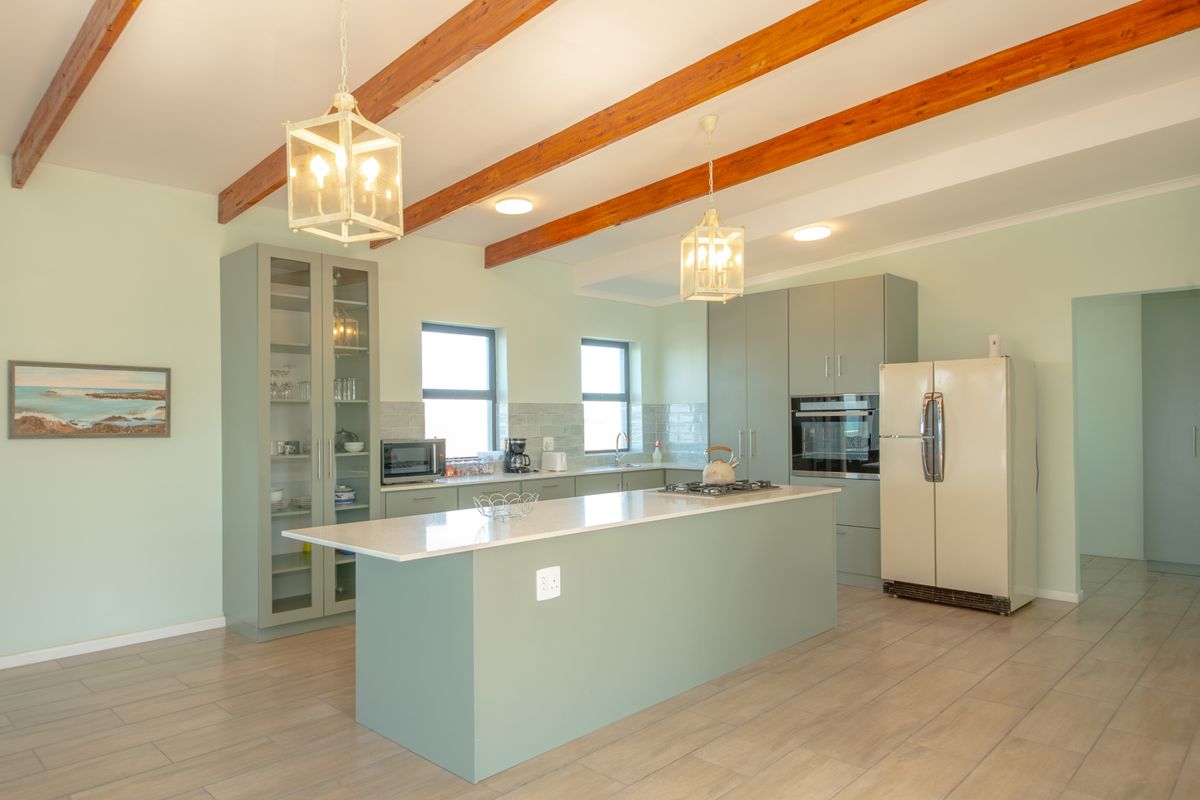 Modern kitchen featuring a central island, stone countertops, sage green cabinetry, exposed timber ceiling beams, and integrated appliances.