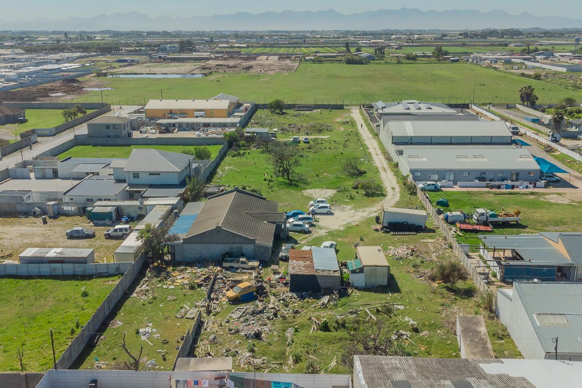 Aerial view of a property plot featuring boundary walls, a main structure with a tiled roof, and significant debris accumulation on the grounds.