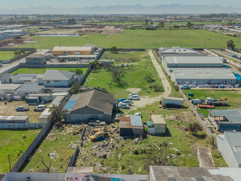 Aerial view of a property plot featuring boundary walls, a main structure with a tiled roof, and significant debris accumulation on the grounds.