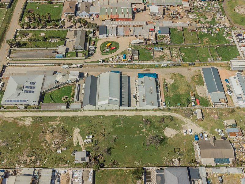 Aerial view of a property complex featuring multiple industrial-style buildings, solar panels, and surrounding land in a semi-developed area.