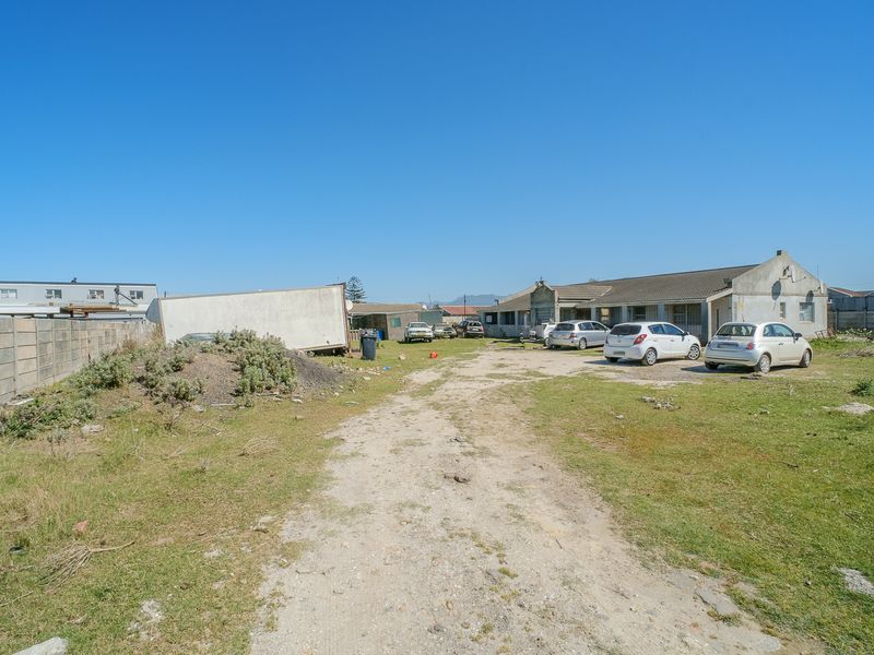 A wide-angle view of the property frontage featuring an unpaved driveway, precast boundary wall, and the main building structure under a clear sky.