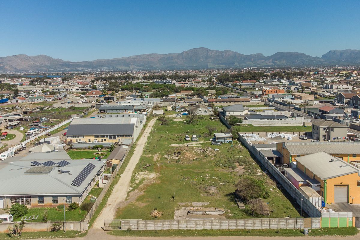 Aerial view of a large, undeveloped plot of land situated within a suburban industrial and residential area, featuring mountain views in the distance.