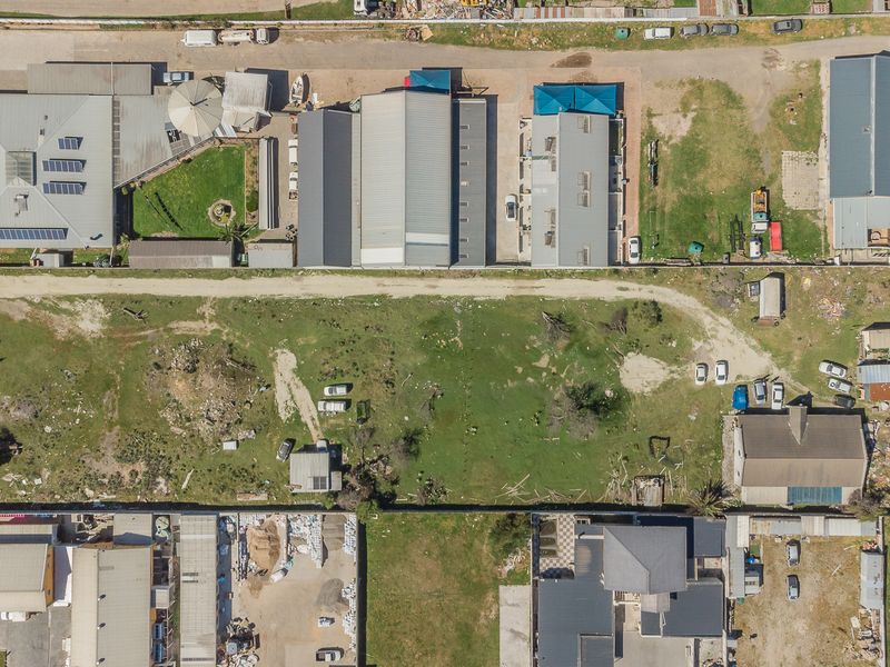 An aerial view of a residential and industrial area showing various building footprints, metal roofs, boundary walls, and open land plots.