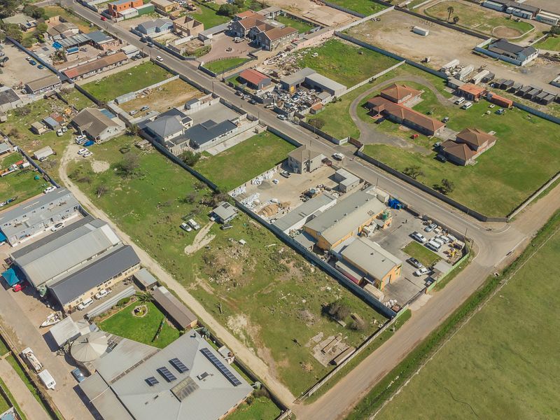 An aerial view of the property and surrounding neighborhood, showcasing the building layout, roof structure, and site access.