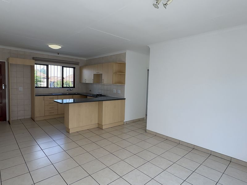 An open-plan living and kitchen area featuring tiled flooring, light wood cabinetry, granite countertops, and a functional kitchen layout with a built-in hob.