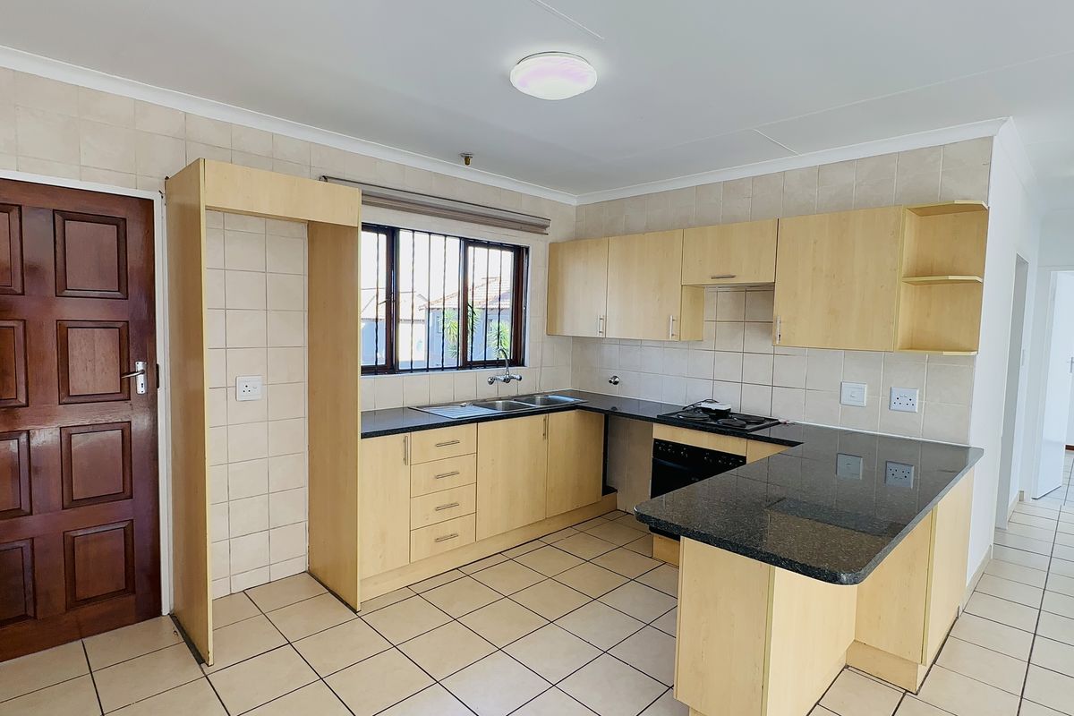 A functional kitchen featuring light wood-finish cabinetry, dark granite countertops, a built-in oven with gas hob, and tiled flooring throughout.