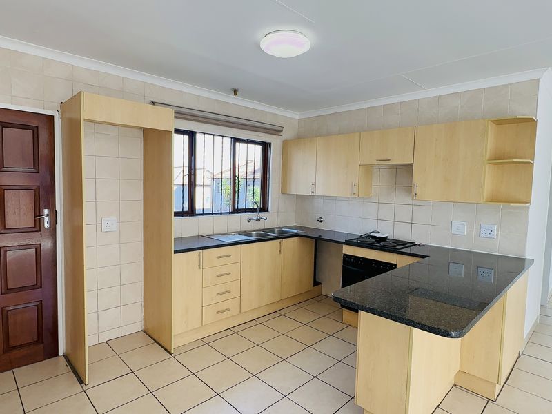 A functional kitchen featuring light wood-finish cabinetry, dark granite countertops, a built-in oven with gas hob, and tiled flooring throughout.