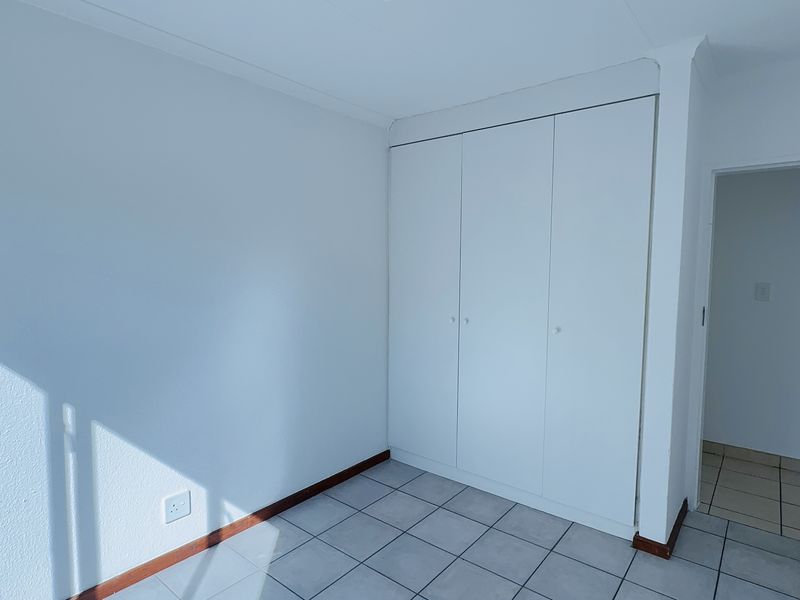 A bright, empty bedroom featuring neutral tiled flooring and built-in cupboards, offering a clean and versatile space ready for personalization.