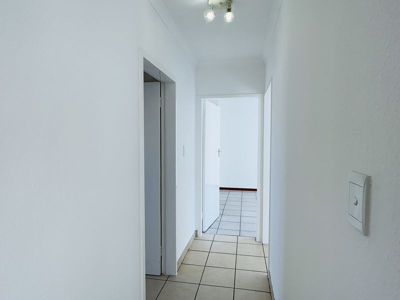 A clean, empty hallway featuring neutral tiled flooring and white walls, providing access to adjacent rooms within the apartment.
