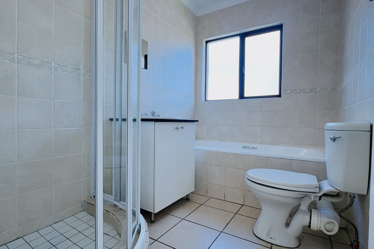 A functional bathroom featuring a shower enclosure, bathtub, vanity cabinet, and toilet with neutral wall and floor tiling.