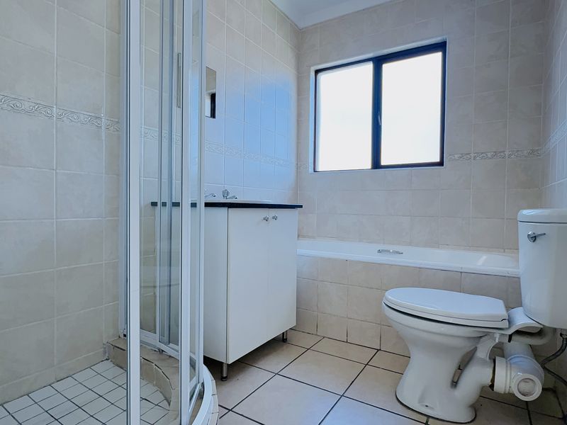 A functional bathroom featuring a shower enclosure, bathtub, vanity cabinet, and toilet with neutral wall and floor tiling.