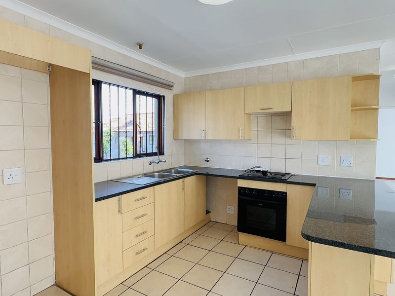 A functional kitchen featuring light wood cabinetry, granite countertops, a built-in oven, gas hob, and tiled finishes throughout.