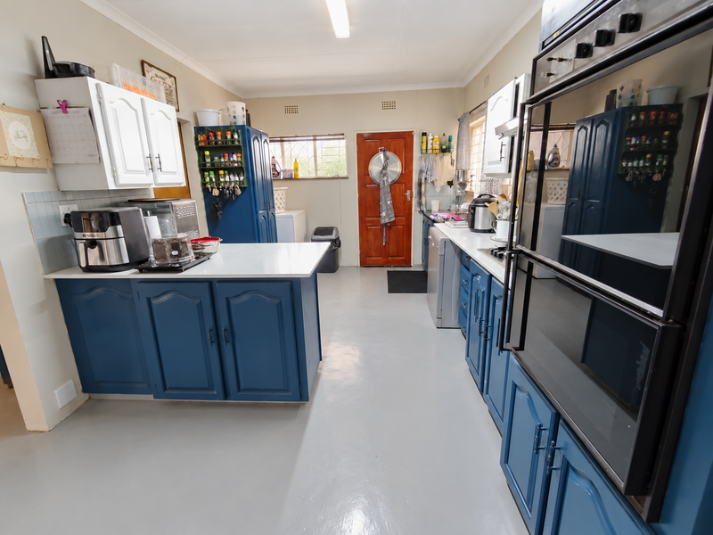 A functional kitchen featuring blue and white cabinetry, a central island, double wall oven, and tiled backsplash with a rear exterior door.