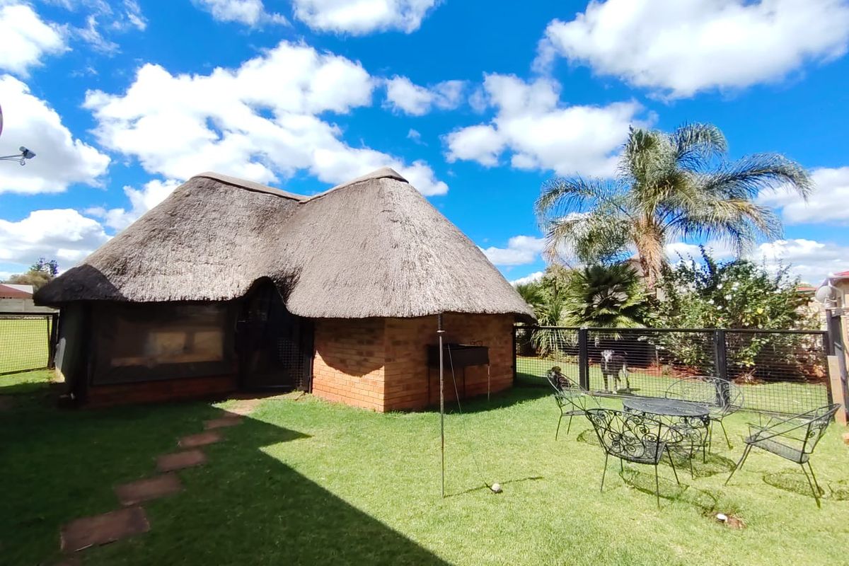 A rear view of a traditional thatch-roofed brick house featuring a well-maintained lawn and secure perimeter fencing.
