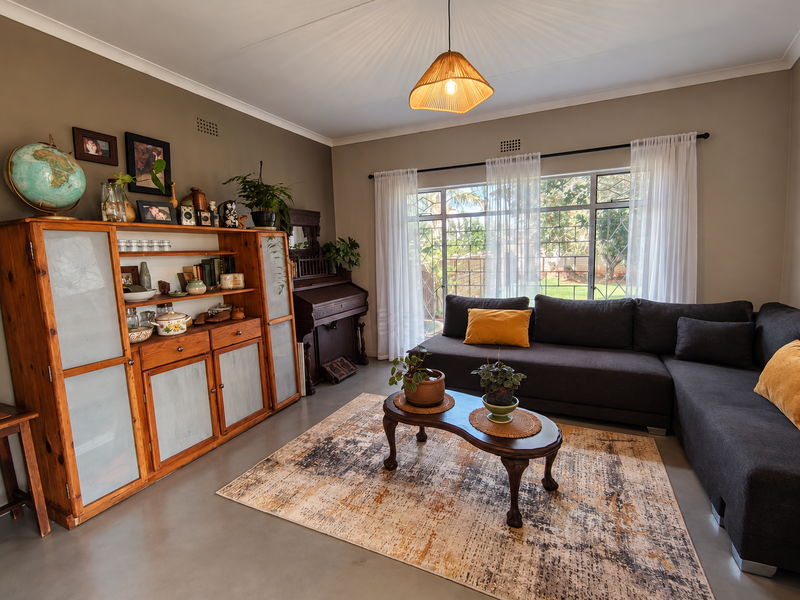 A well-maintained living room featuring polished concrete floors, large windows with security bars, and neutral wall tones, creating a comfortable and inviting atmosphere.