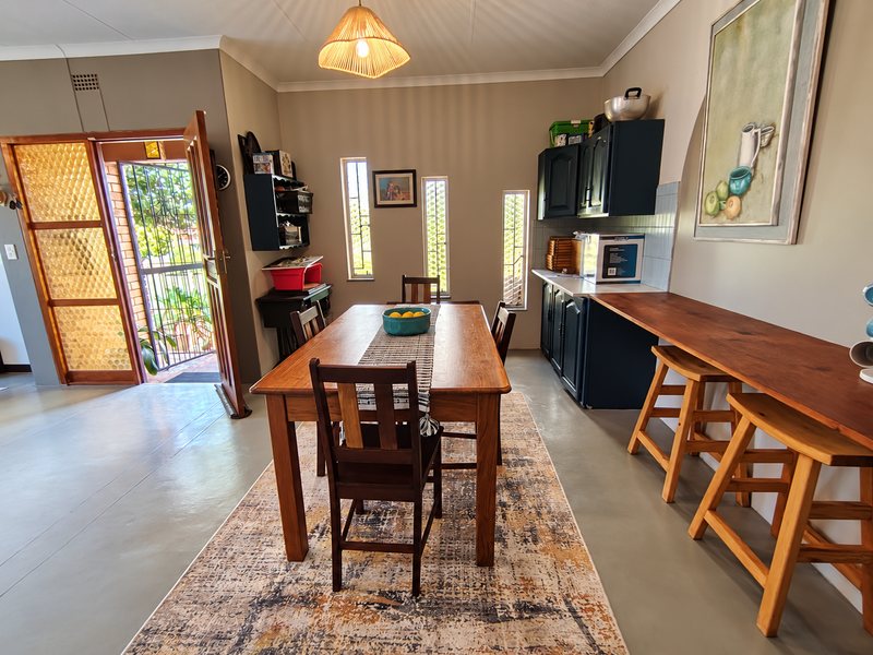 An open-plan dining and kitchen area featuring dark cabinetry, a timber breakfast bar, and direct access to the exterior through a security door.