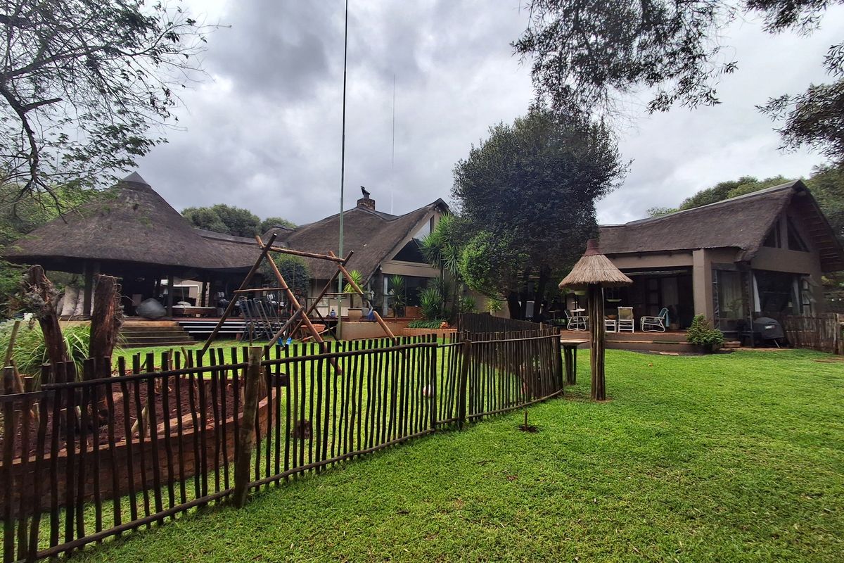 Spacious rear garden featuring a well-maintained lawn, wooden fencing, and multiple covered patio areas under traditional thatch roofing.