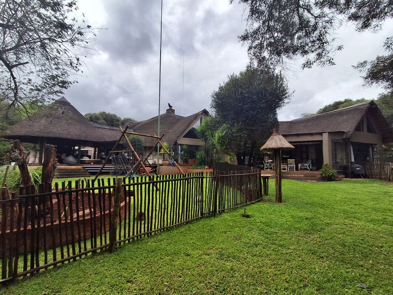 Spacious rear garden featuring a well-maintained lawn, wooden fencing, and multiple covered patio areas under traditional thatch roofing.