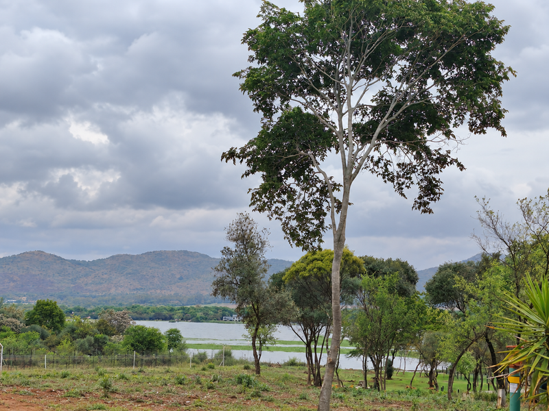 Scenic landscape view featuring mature trees, open grounds, and a distant lake set against a backdrop of rolling hills.